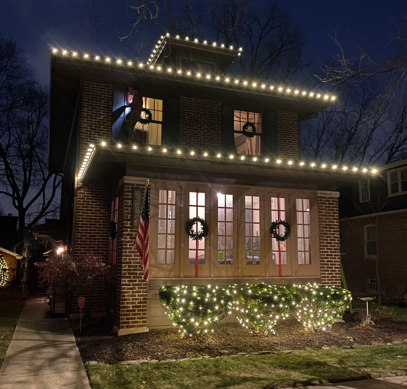 Warm-white eave lighting with coordinated shrubs and front-entry details