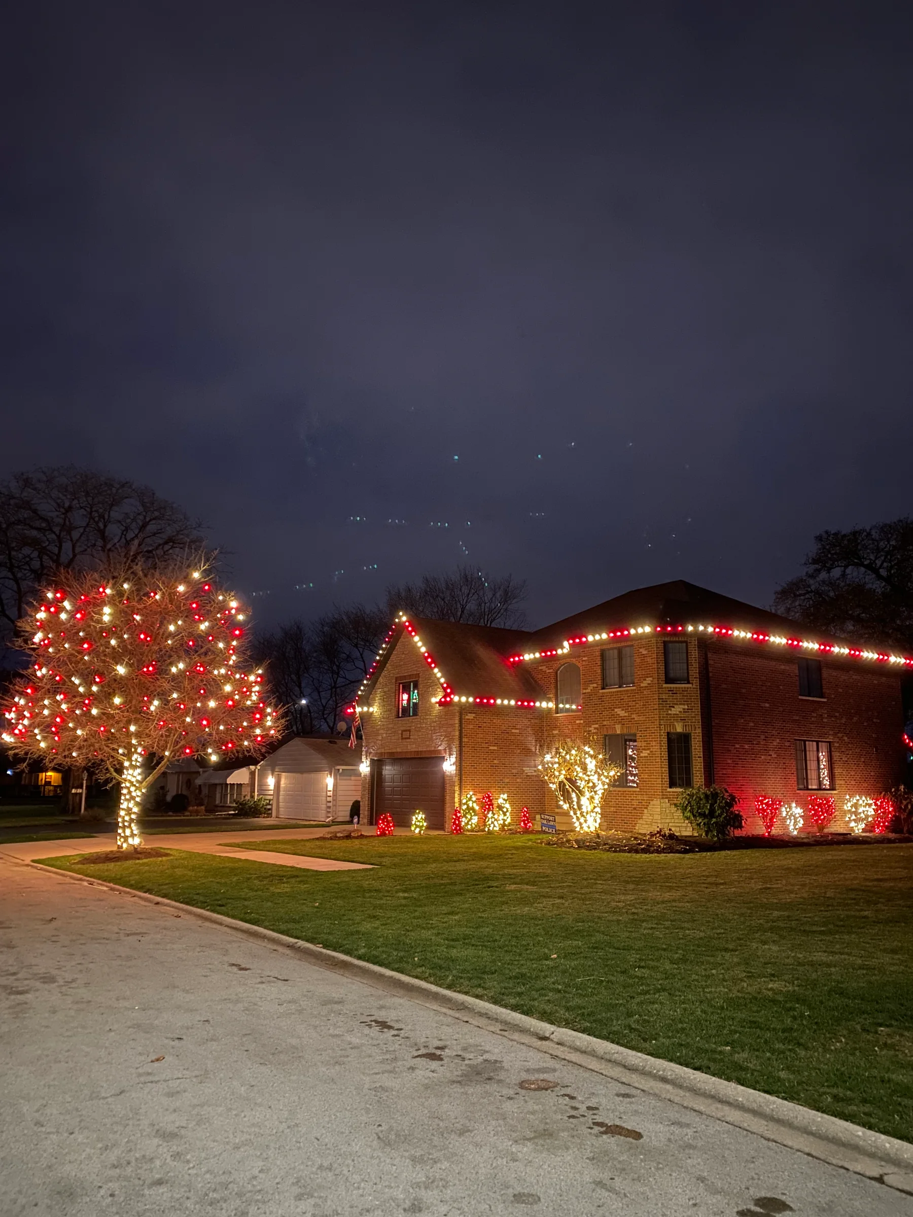 Broad brick home with red and white roofline and landscape lights